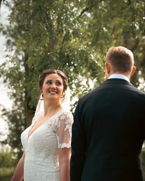 Bruid kijkt lachend om naar de bruidegom onder een boom